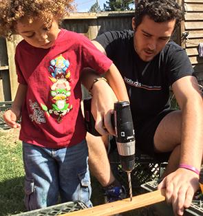 Young boy being taught how to use a drill